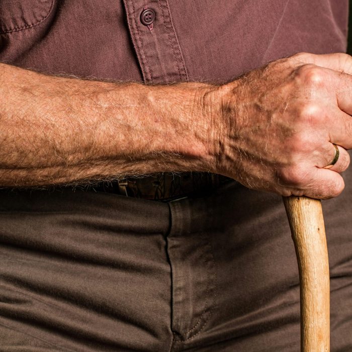 Close Up Of A Senior Adult's Hand Gripping A Wooden Walking Cane Outdoors, Symbolizing Support And Aging.