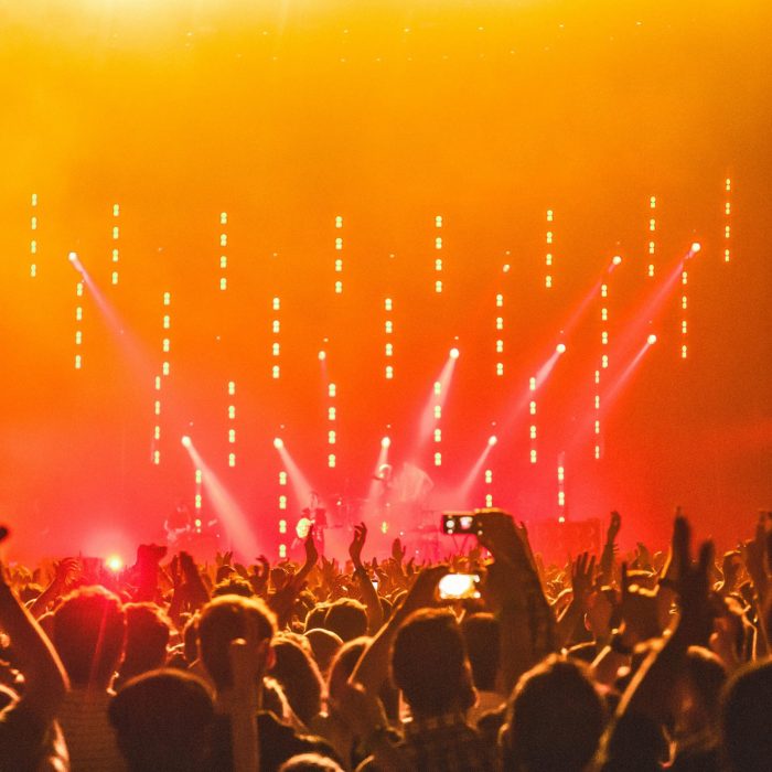 Energetic Crowd At A Live Concert With Bright Stage Lights And Hands Raised In Celebration.