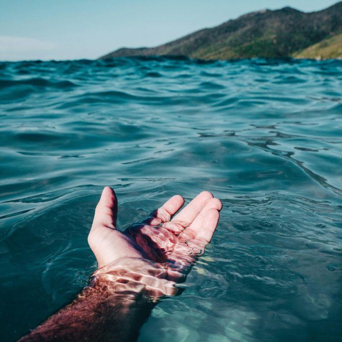 A Serene Hand Emerges From The Vibrant Ocean Waves At Arraial Do Cabo Under Daylight.