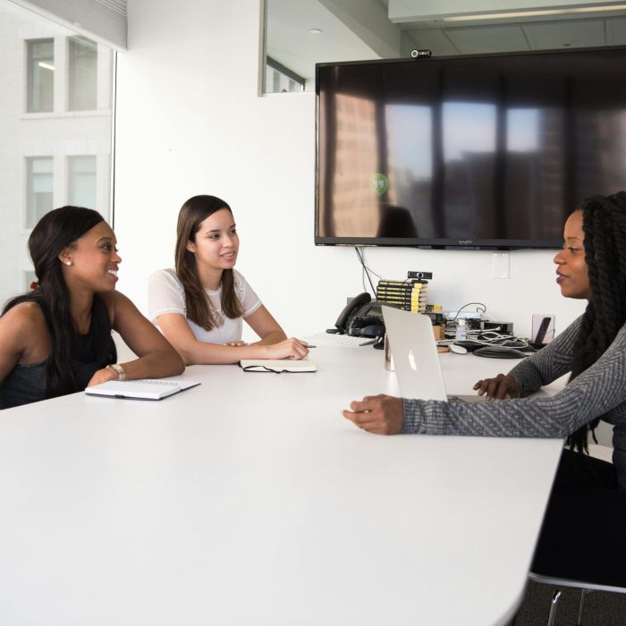 Three Women Collaborate In A Modern Office Setting, Discussing Business Plans And Teamwork.