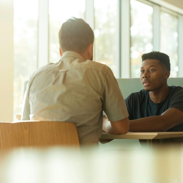 Two Men Sitting At A Table In A Modern Office Space During The Day.