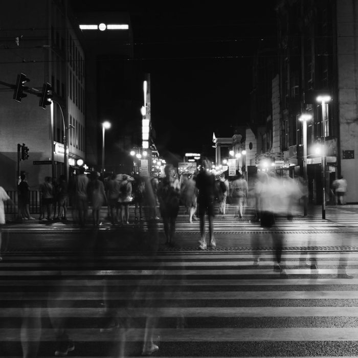 A Bustling Nighttime City Scene With Blurred Pedestrians Crossing A Street Under Urban Lights.