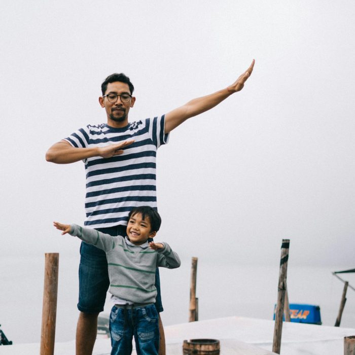 Father And Son Posing Playfully On A Wooden Dock By The Water, Enjoying A Day Outdoors.