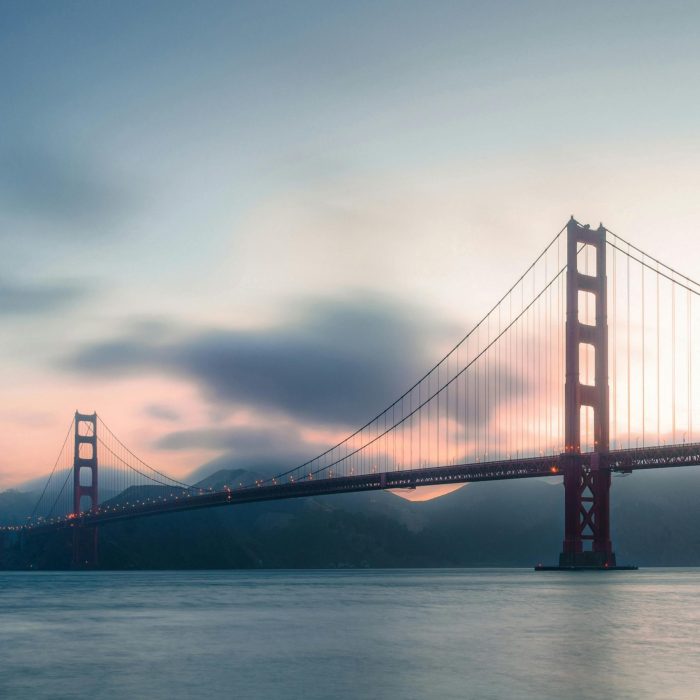 Stunning Sunset View Of The Iconic Golden Gate Bridge In San Francisco Over Calm Ocean Waters.