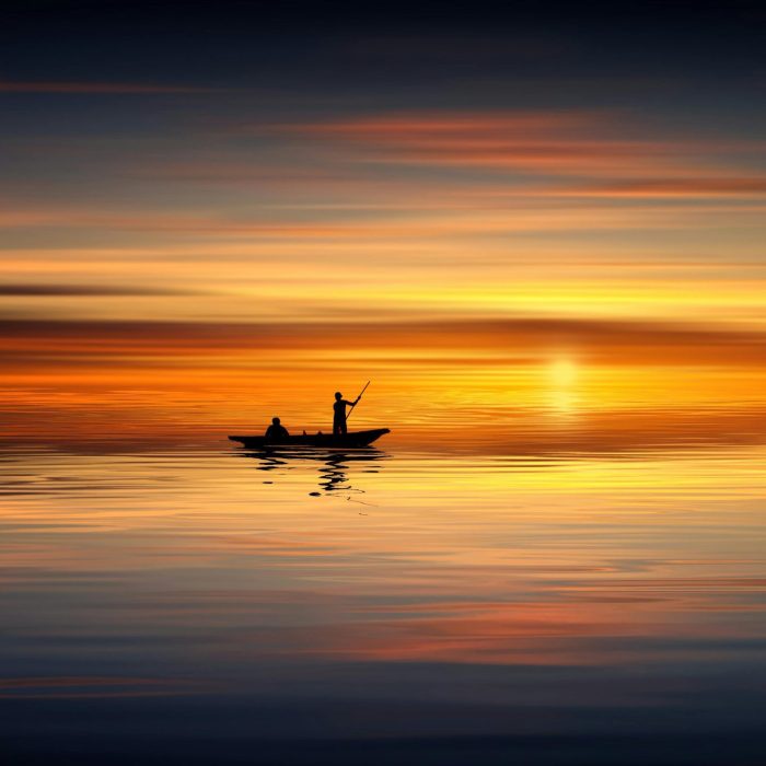 Silhouette Of Two People In A Boat Against A Vibrant Sunset Over Calm Waters. Tranquil Scene.
