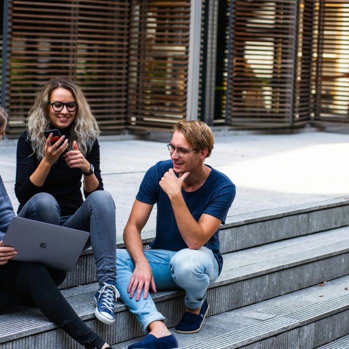 Three Young Professionals Having A Friendly Chat While Sitting On Outdoor Steps.