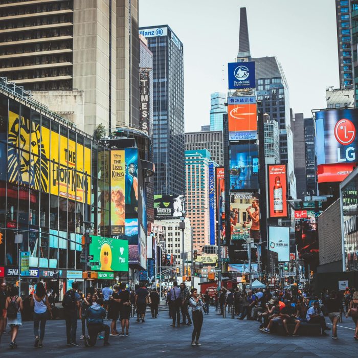 Bustling Daytime View Of Times Square With Crowds, Skyscrapers, And Iconic Billboards In New York City.