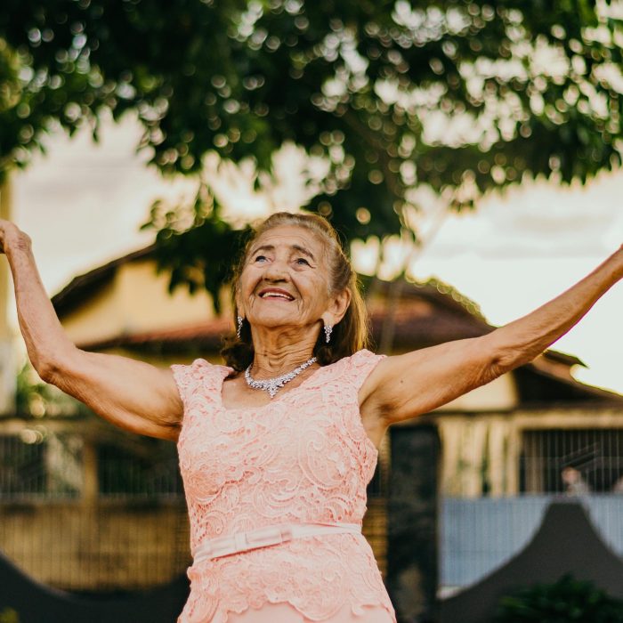 Elderly Woman In A Pink Lace Dress Smiling And Posing Outdoors.