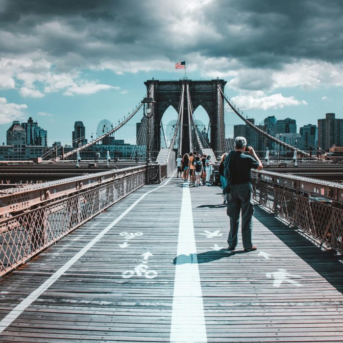 Iconic View Of Brooklyn Bridge Filled With Pedestrians Under Dramatic Skies.