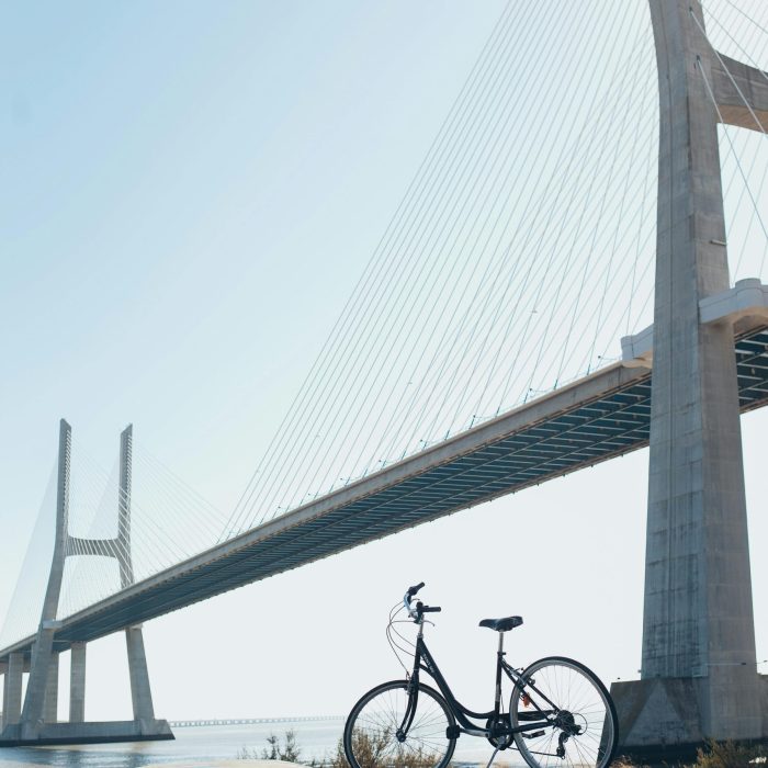 A Bicycle With Vibrant Graffiti Beneath A Striking Suspension Bridge Under A Clear Blue Sky.