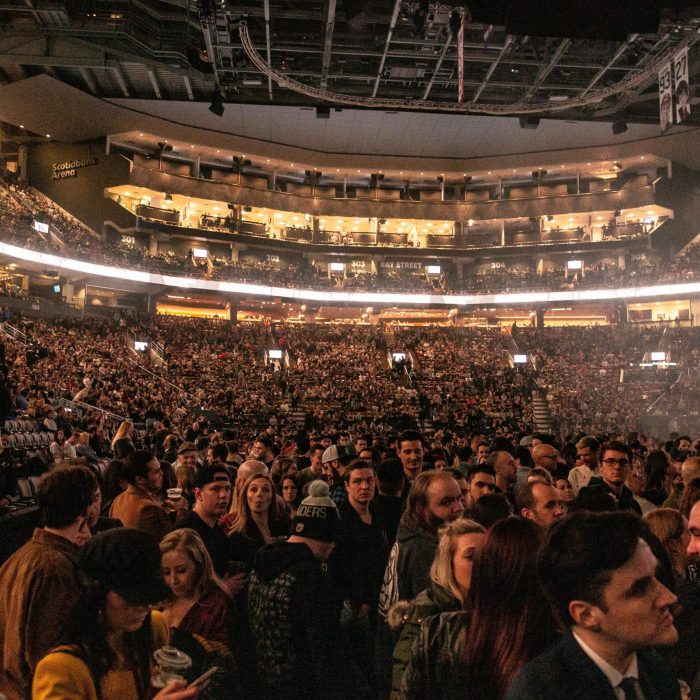 A Large Crowd Gathers In An Indoor Arena For A Lively Event, Surrounded By Bright Lights.