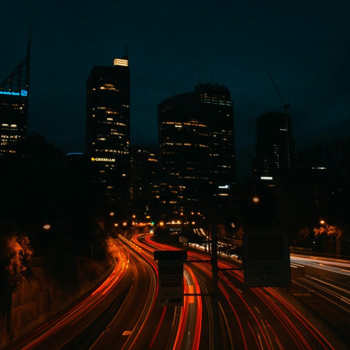 Urban Night Scene Capturing Light Trails On A Highway Under A Dark Sky, Showcasing City Skyscrapers.