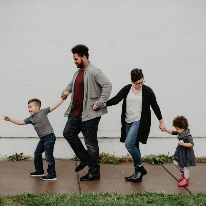 A Joyful Family Walking Together Outdoors, Holding Hands In A Playful And Happy Moment.