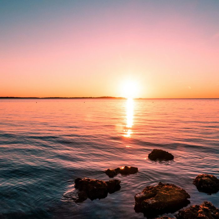 Experience The Serene Beauty Of A Sunset In Peroj, Overlooking The Adriatic Sea With Rocky Shores.