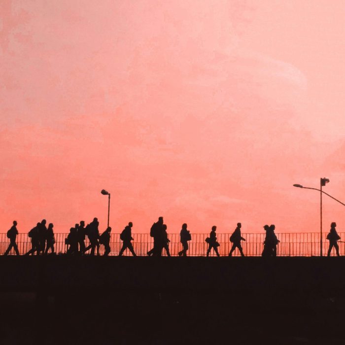 Dramatic Silhouettes Of People Walking Across A Bridge Against A Warm Sunset Sky.