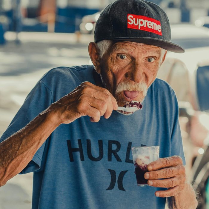 Senior Man Savoring A Sweet Treat Outdoors, Wearing A Trendy Cap And Casual Outfit.