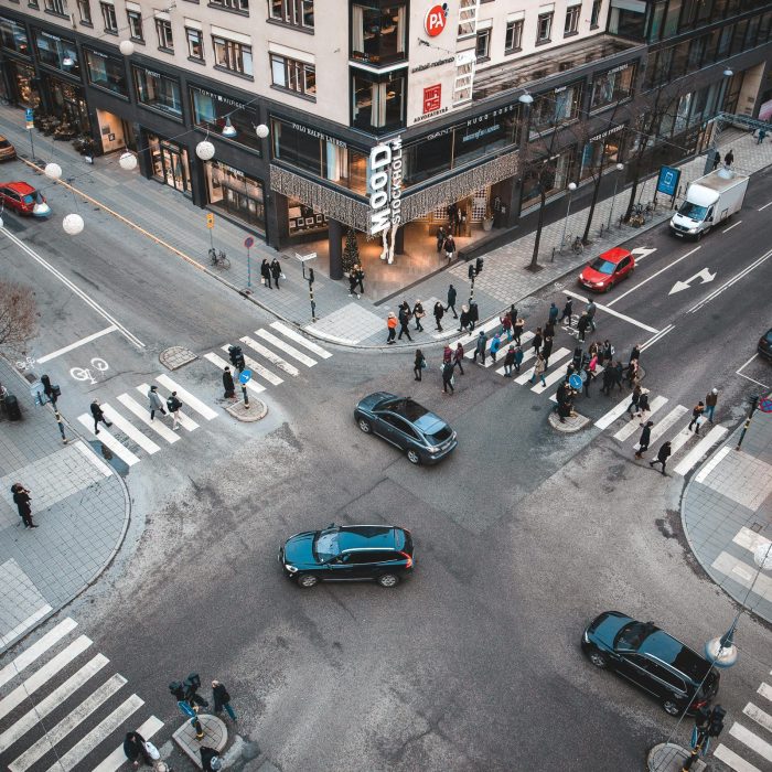 A Bustling Stockholm Street Intersection With Pedestrians And Vehicles On A Sunny Day.