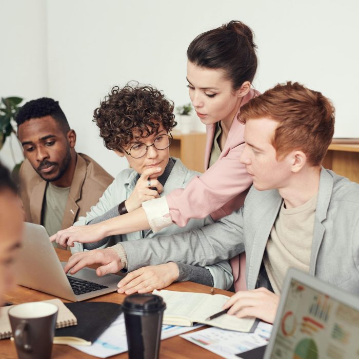 A Group Of Professionals Engaged In A Collaborative Office Meeting, Discussing Ideas With Laptops.