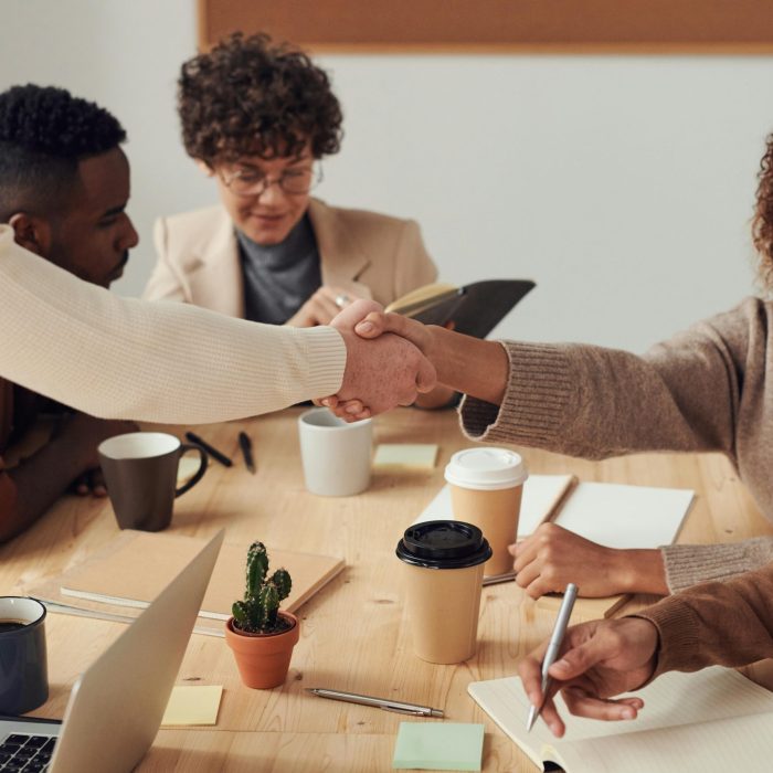 Colleagues Collaborating Indoors, Sharing Smiles, And Shaking Hands During A Business Meeting.