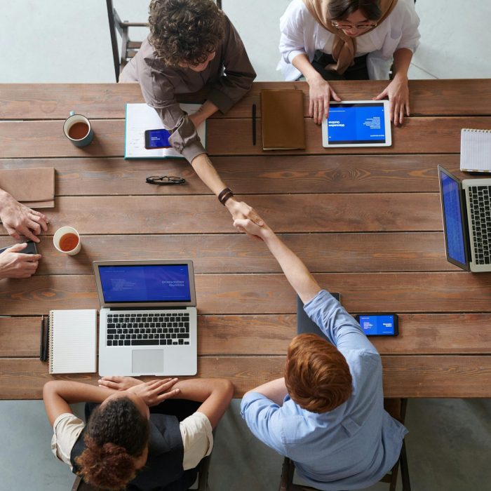 Overhead View Of Colleagues In A Work Meeting Using Laptops And Tablets, Emphasizing Teamwork And Technology.