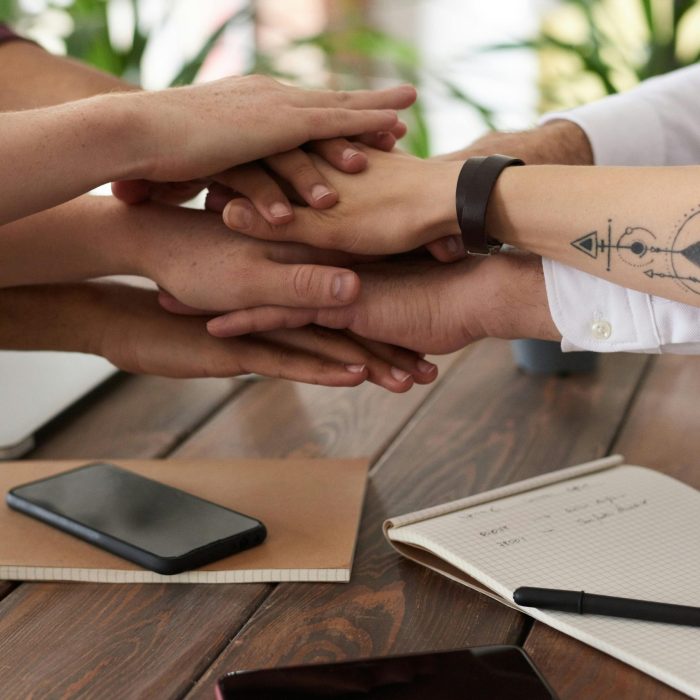 Hands From A Diverse Team Stack On A Table Symbolizing Unity And Teamwork In A Modern Office Setting.
