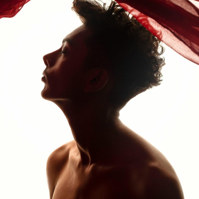 Silhouette Of A Topless Man With Flowing Red Fabric. Dramatic Lighting Creates An Artistic Mood.