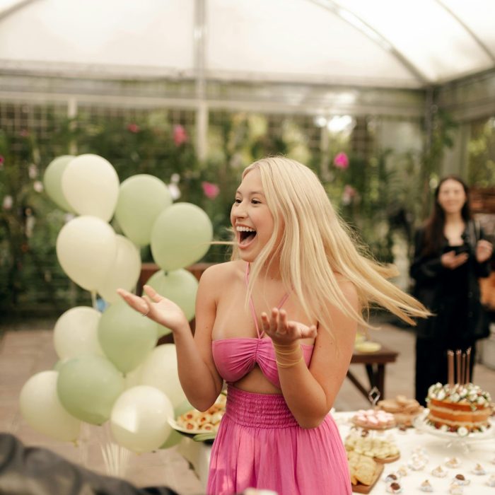 A Joyful Woman In A Pink Dress Celebrates At An Indoor Party With Balloons And Desserts.