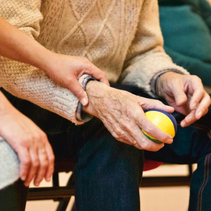 An Elderly Person Receives Support From A Caregiver, Holding Hands Indoors, Showcasing Compassion.