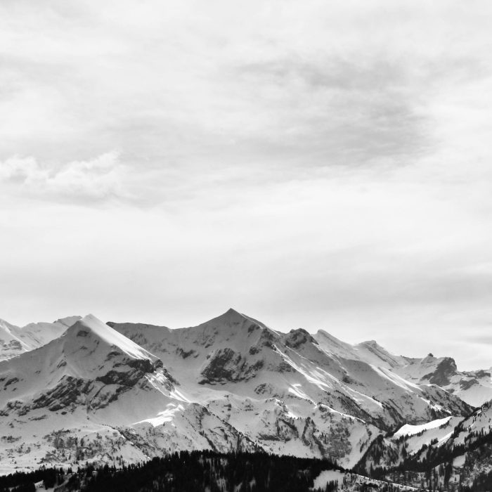 Stunning Monochrome Landscape Of Snow Covered Alpine Mountains Under A Cloudy Sky.