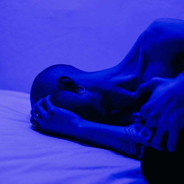A Tattooed Man Lying In Blue Light, Symbolizing Isolation And Stress.