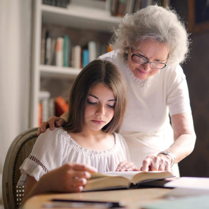 A Grandmother And Young Girl Reading A Book Together In A Cozy Indoor Setting, Fostering Education And Bonding.
