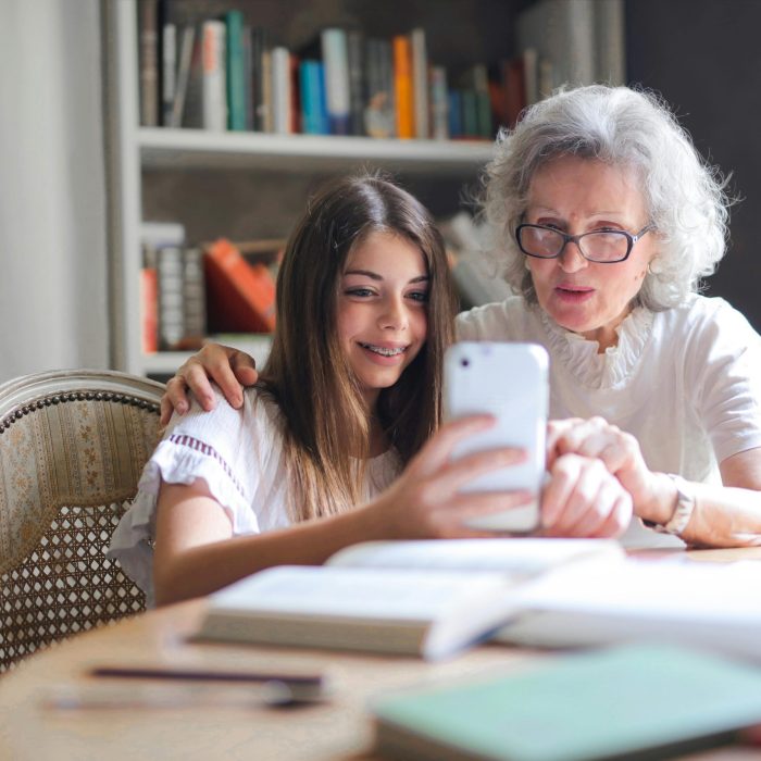 A Grandmother And Granddaughter Bonding Over A Smartphone At Home, Showcasing Generational Connection.