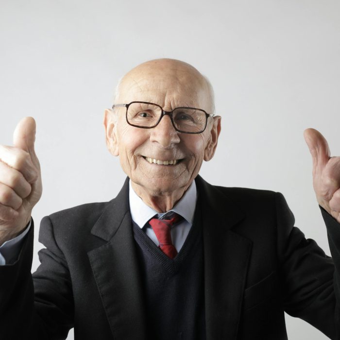 Cheerful Elderly Man In Suit Giving Thumbs Up, Symbolizing Success And Approval.