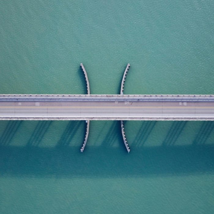 Aerial Shot Of A Bridge Over Clear Blue Water, Showcasing Modern Architecture And Symmetry.