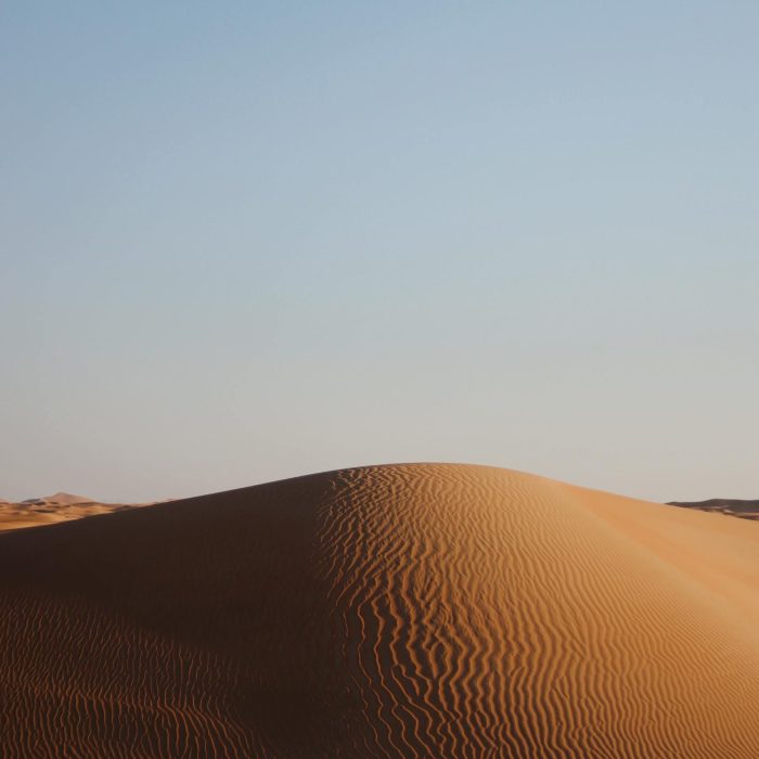 Captivating View Of A Sunlit Sand Dune With Clear Blue Sky Background, Showcasing Natural Desert Beauty.