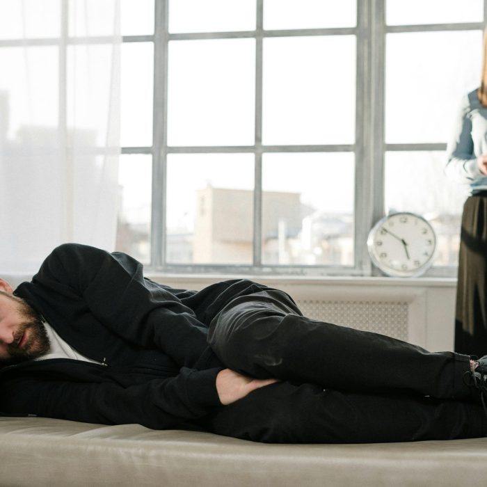 Psychological Therapy Session With A Male Patient Lying On A Couch And A Female Therapist Taking Notes.