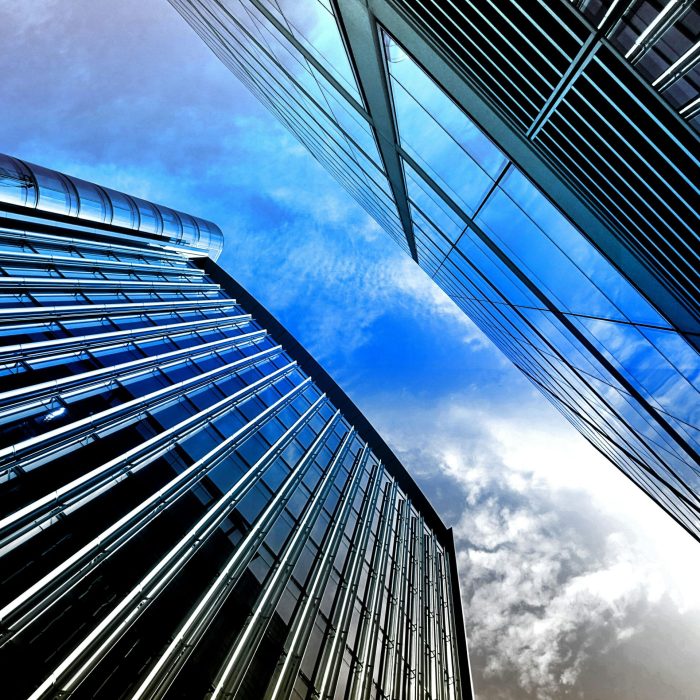 Low Angle View Of Modern Skyscrapers With Reflective Glass Against A Bright Blue Sky.