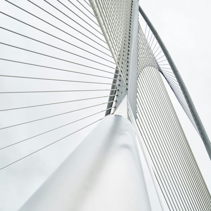Low Angle View Of A Modern Suspension Bridge With Steel Cables And Architectural Lines Under A Cloudy Sky.