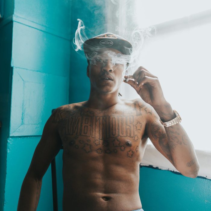 A Tattooed Man Smoking In A Vibrant Blue Indoor Space, Creating An Artistic Vibe.