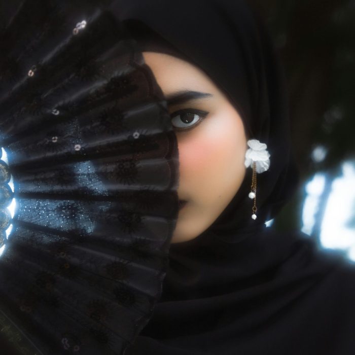 Portrait Of A Young Woman In A Black Hijab Holding A Fabric Fan.