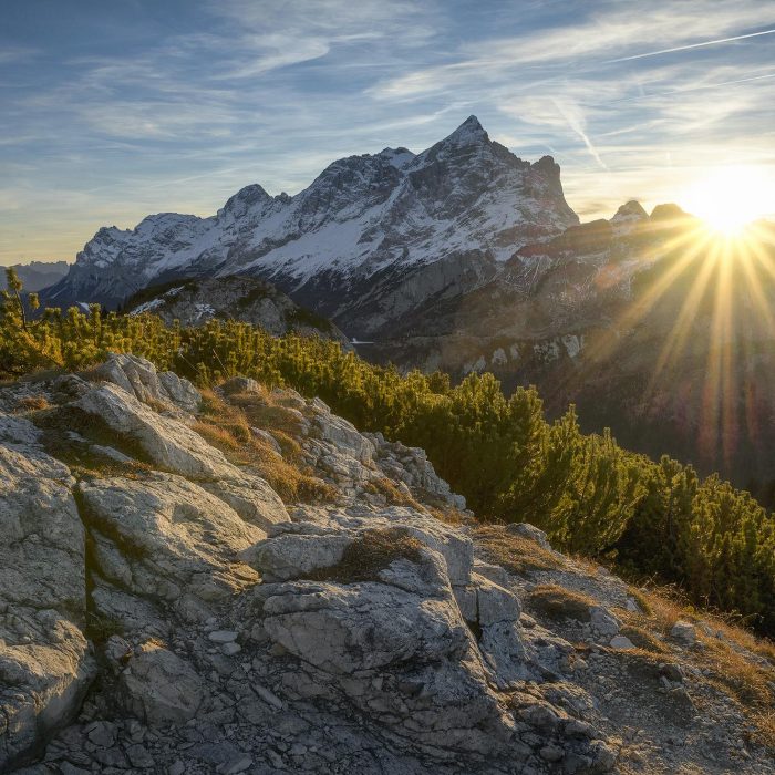 Stunning Sunrise Casting Rays Over The Italian Alps In Alleghe, Veneto, With Lush Greenery And Rocky Terrain.