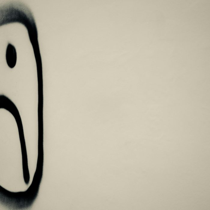 A Monochrome Photo Of A Sad Face Graffiti On A Wall, Symbolizing Urban Emotion.