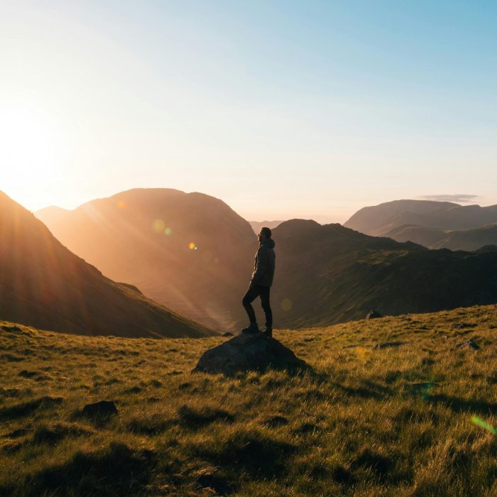 Silhouette Of A Person Standing On A Hill During Sunrise In Cumbria, England With Scenic Mountain Views.