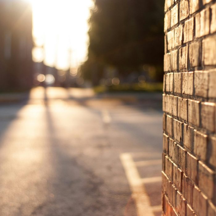 Close Up Of A Sunlit Brick Wall With Blurred Urban Street In The Background At Sunset.
