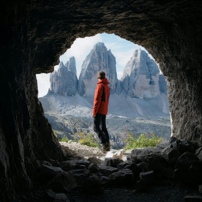 Man In Red Jacket Standing In Cave Entrance, Viewing Tre Cime Di Lavaredo In Italy.