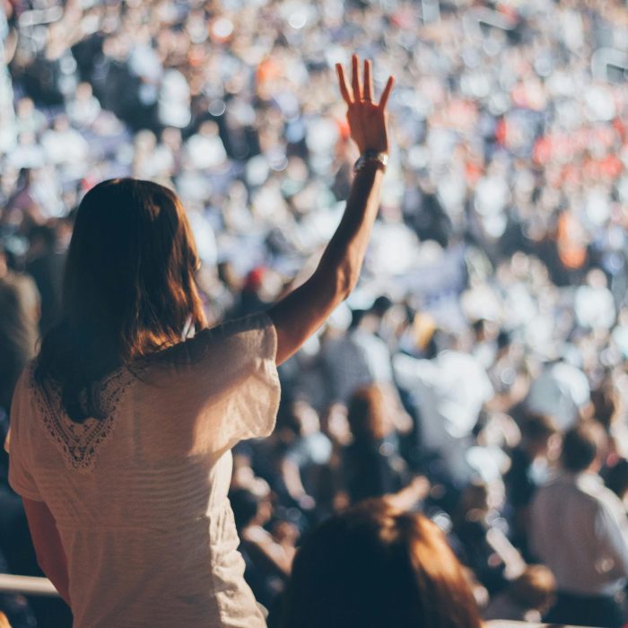 Diverse Crowd Enjoying A Live Event With One Woman Raising Her Hand In Excitement.