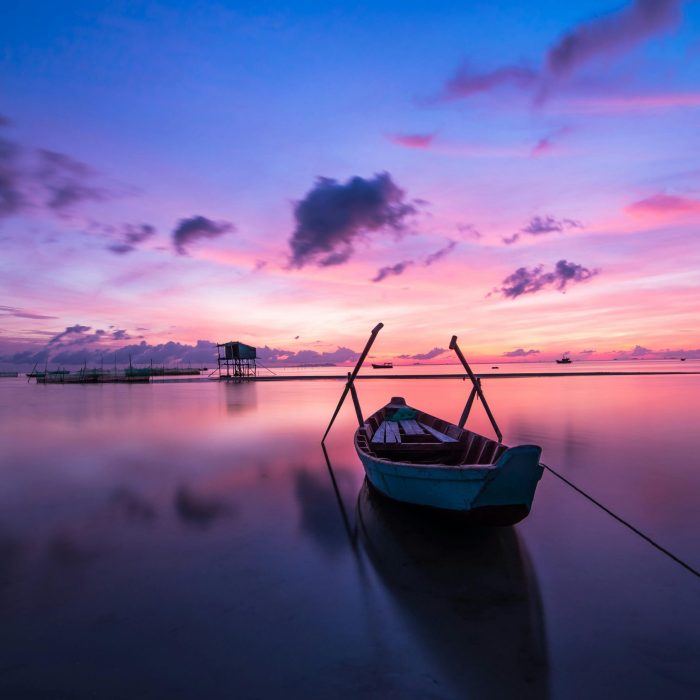 A Tranquil Tropical Sunrise With A Lone Boat On Calm Waters.