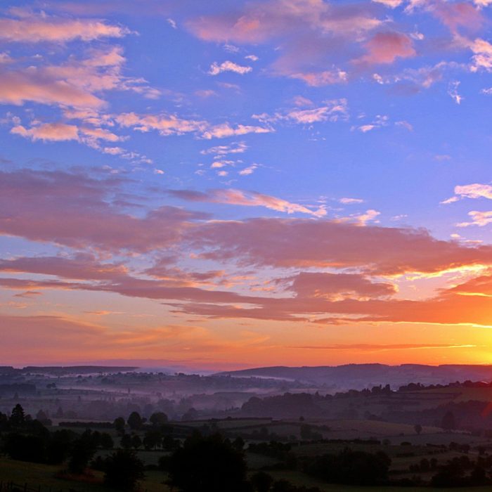 Stunning Sunrise Over Rolling Hills With Colorful Clouds And A Vivid Skyscape.